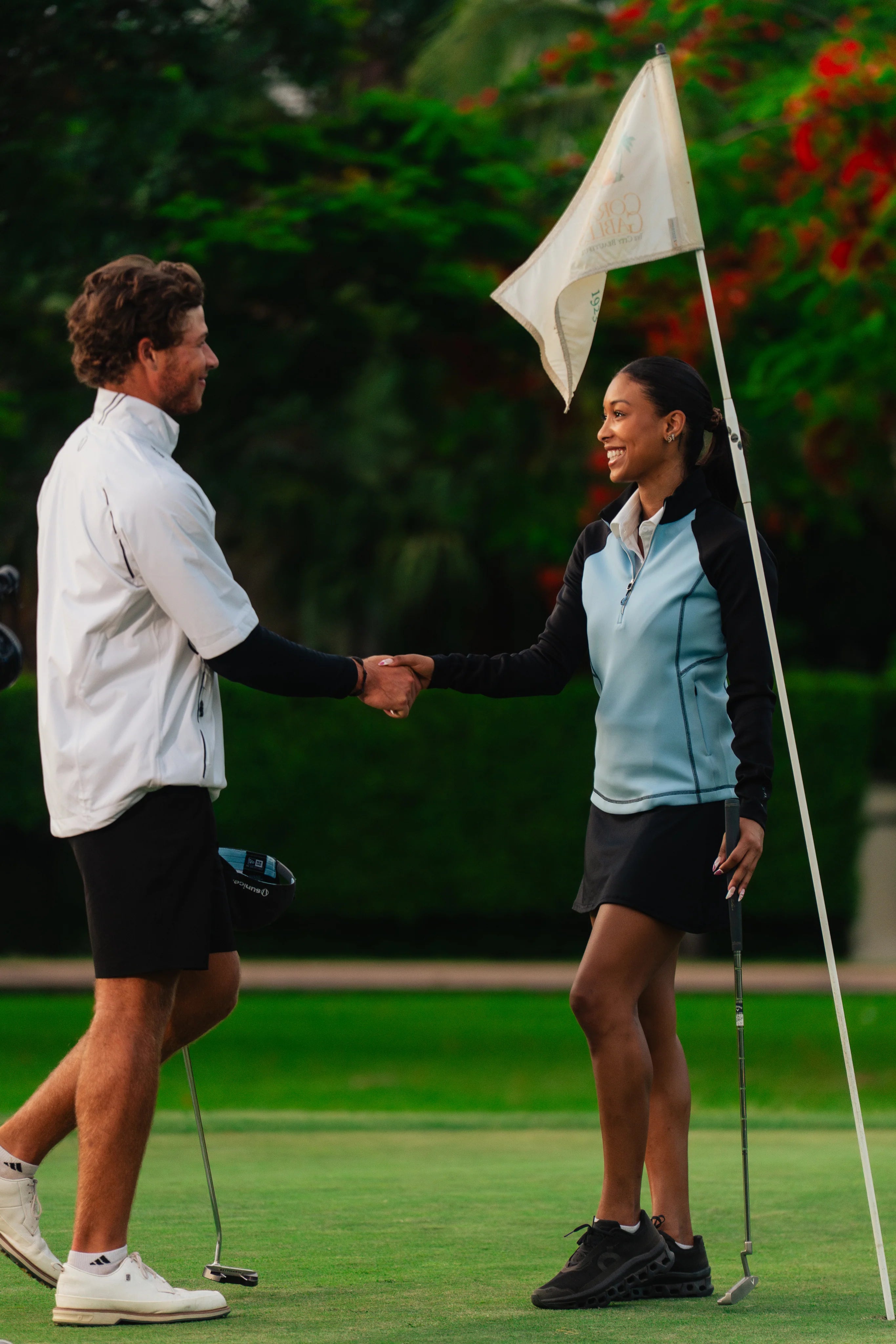 Two golfers shaking hands on a golf course with a flag in the background.