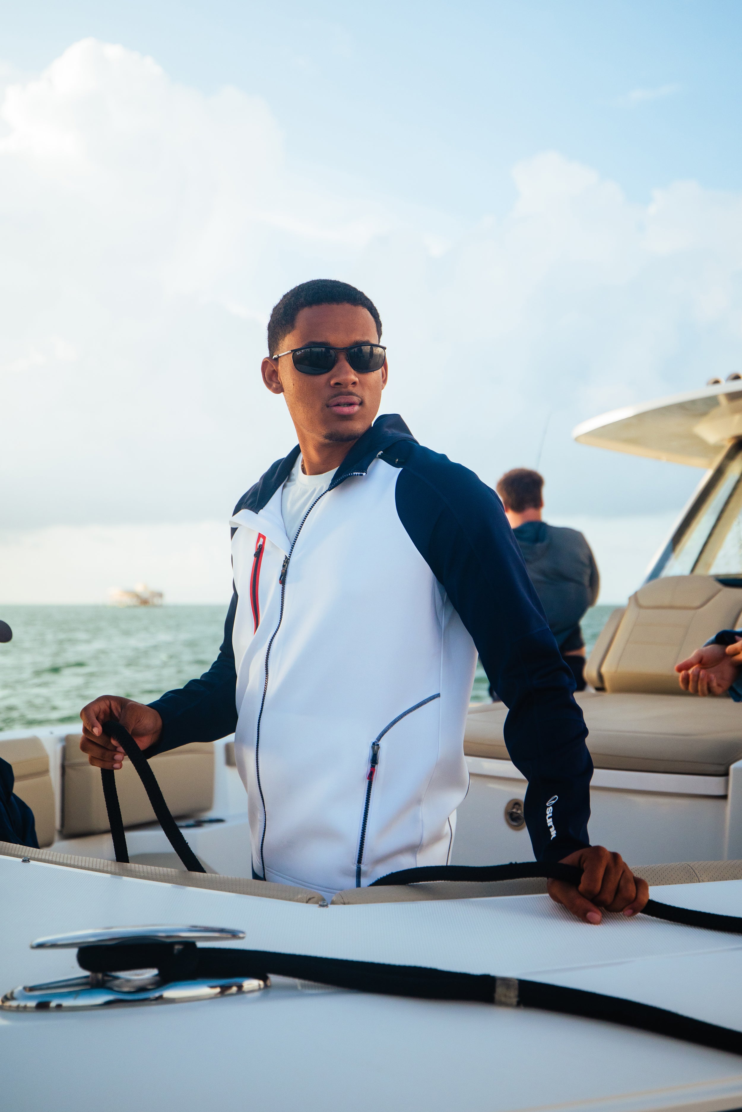 Man holding a rope on a boat with a clear sky and water background where a Sunice Element Shield jacket.
