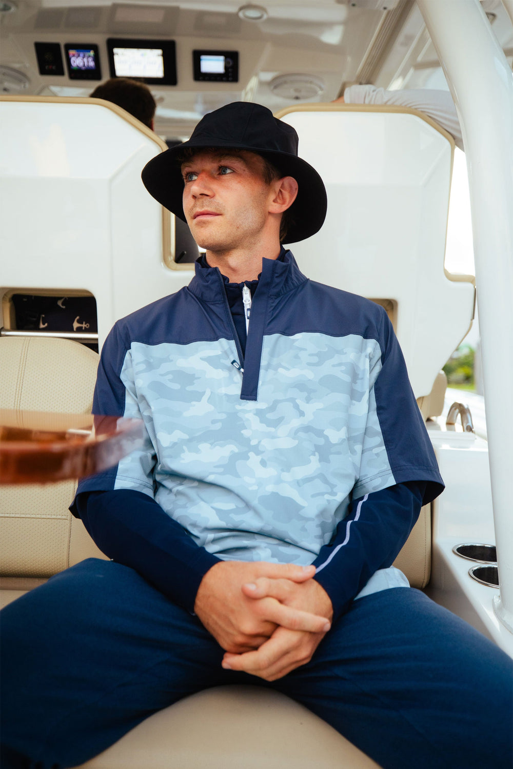 Man wearing a two tone blue Sunice pullover with a black Sunice bucket hat on a boat