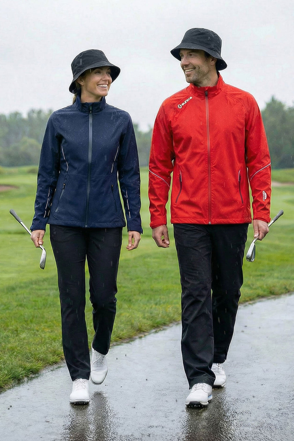 Two people walking on a golf course in raincoats holding golf clubs.