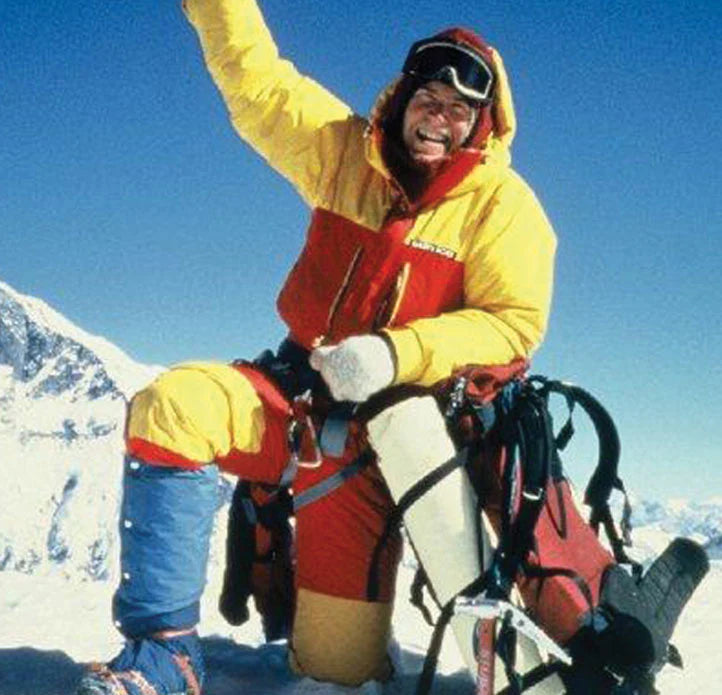Person in red and yellow winter clothing with climbing gear on a snowy mountain
