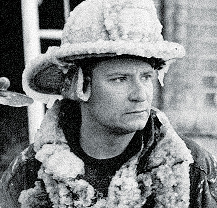 Firefighter wearing a snow-covered helmet and coat in a cold environment