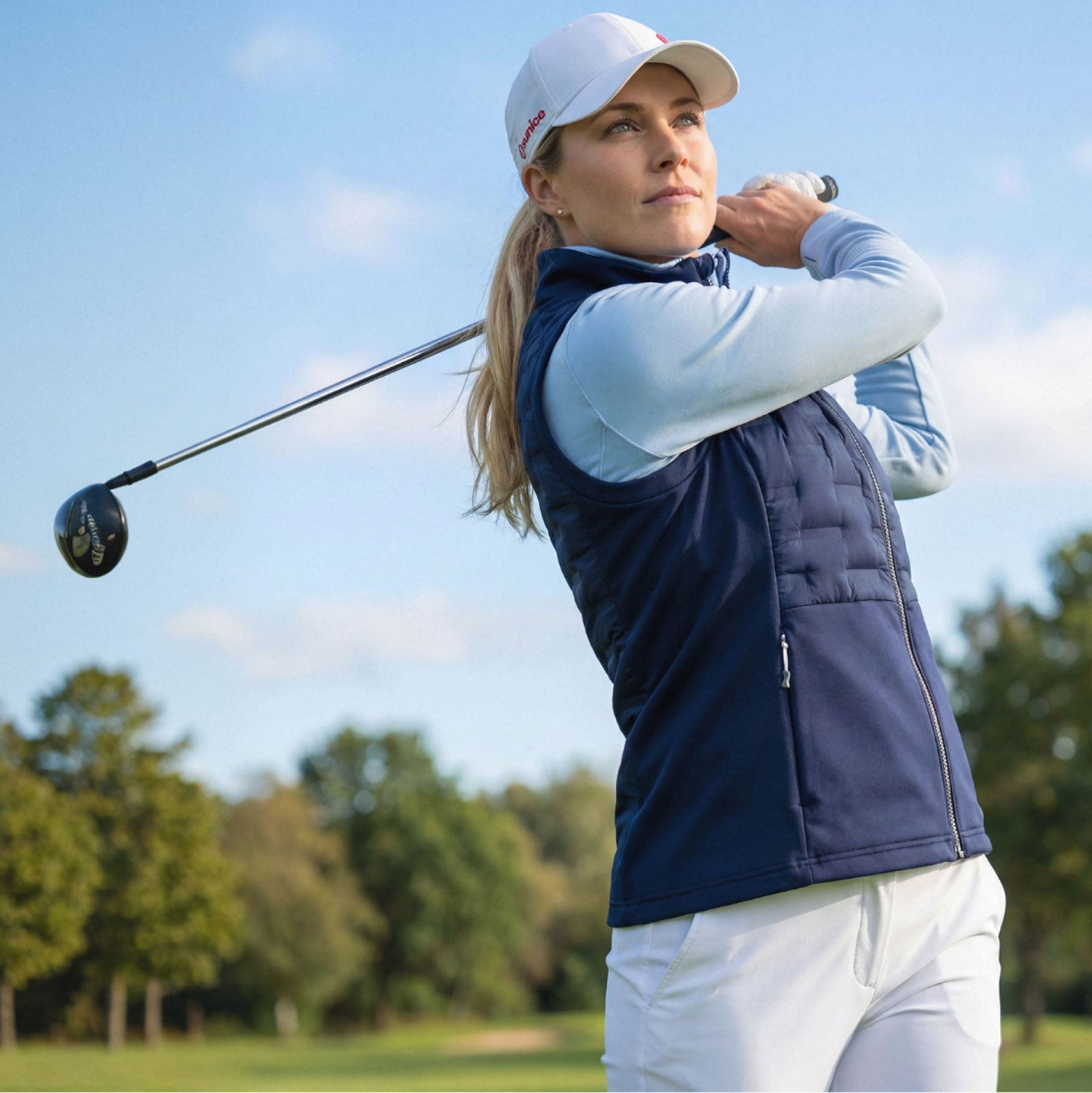Woman playing golf on a sunny day with trees in the background